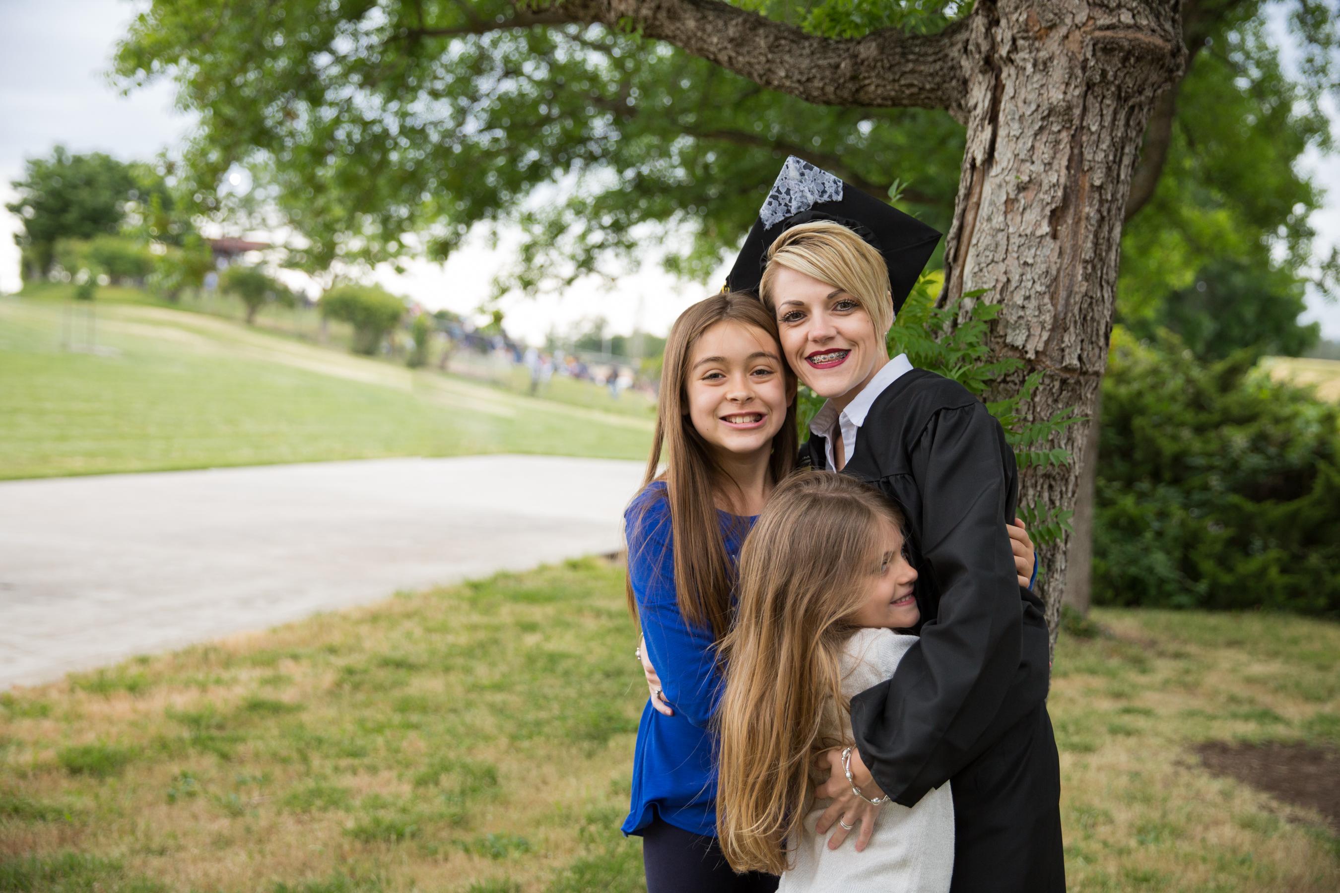 female student in cap and gown hugging two daughters